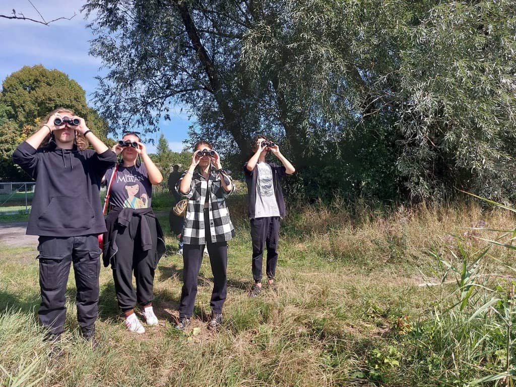 Zdjęcie przedstawia młodzież z lornetkami obserwującą przyrodę