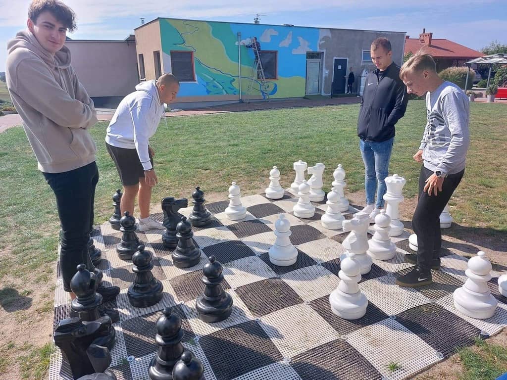 Zdjęcie przedstawia młodzież grającą w plenerowe szachy